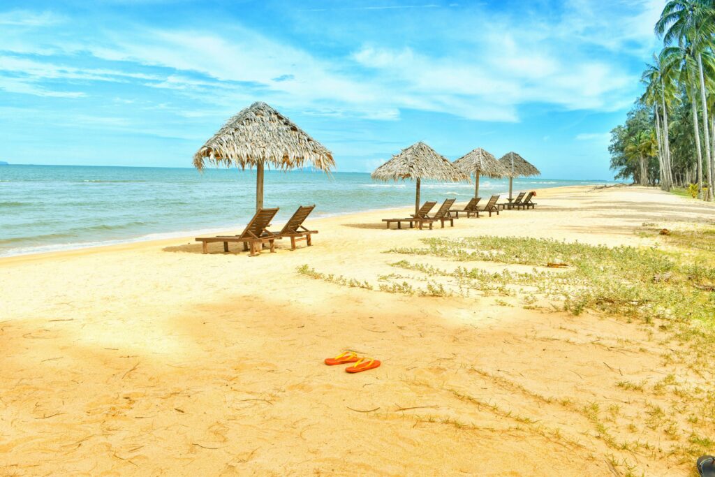 Idyllic tropical beach scene with empty lounge chairs under straw umbrellas on a sunny day.